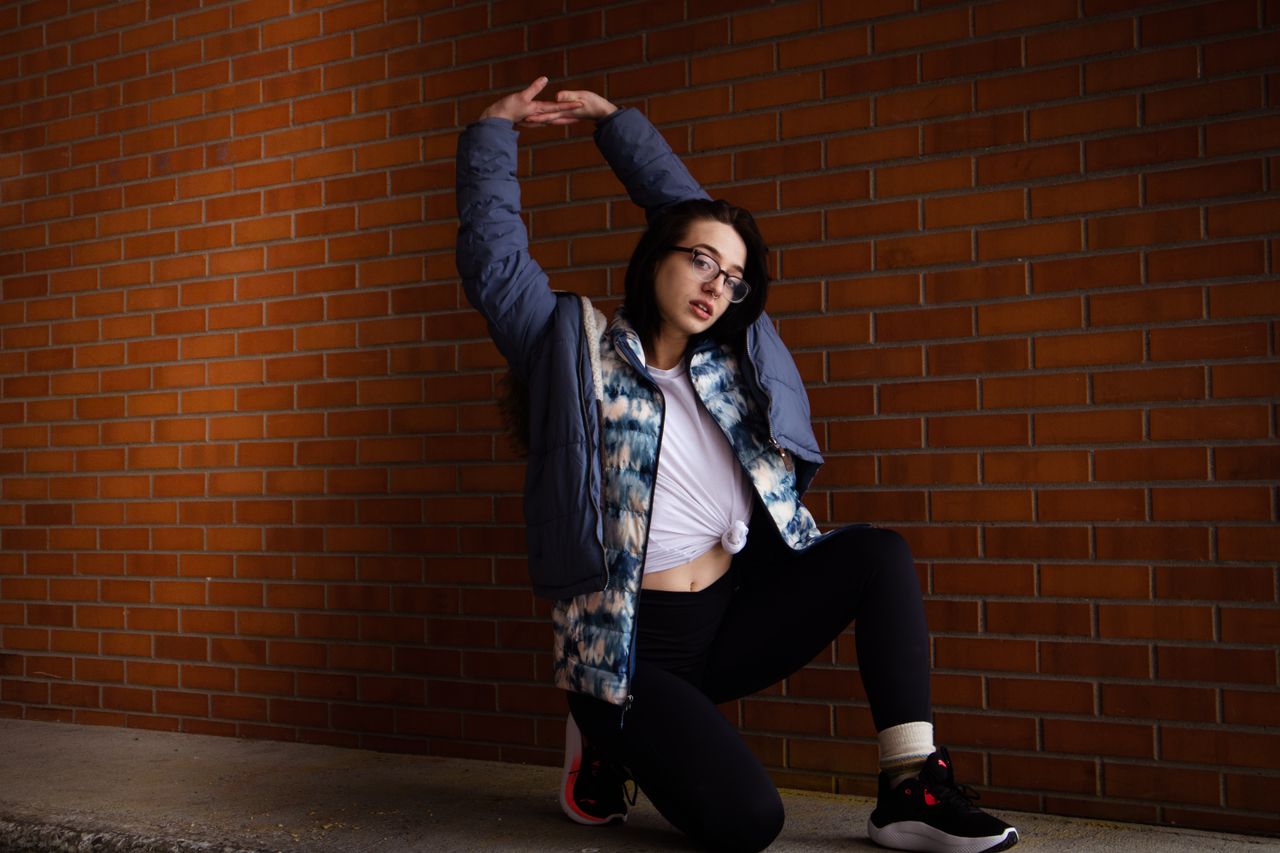who-we-are Stylish woman poses confidently against a brick wall, showcasing modern casual fashion.