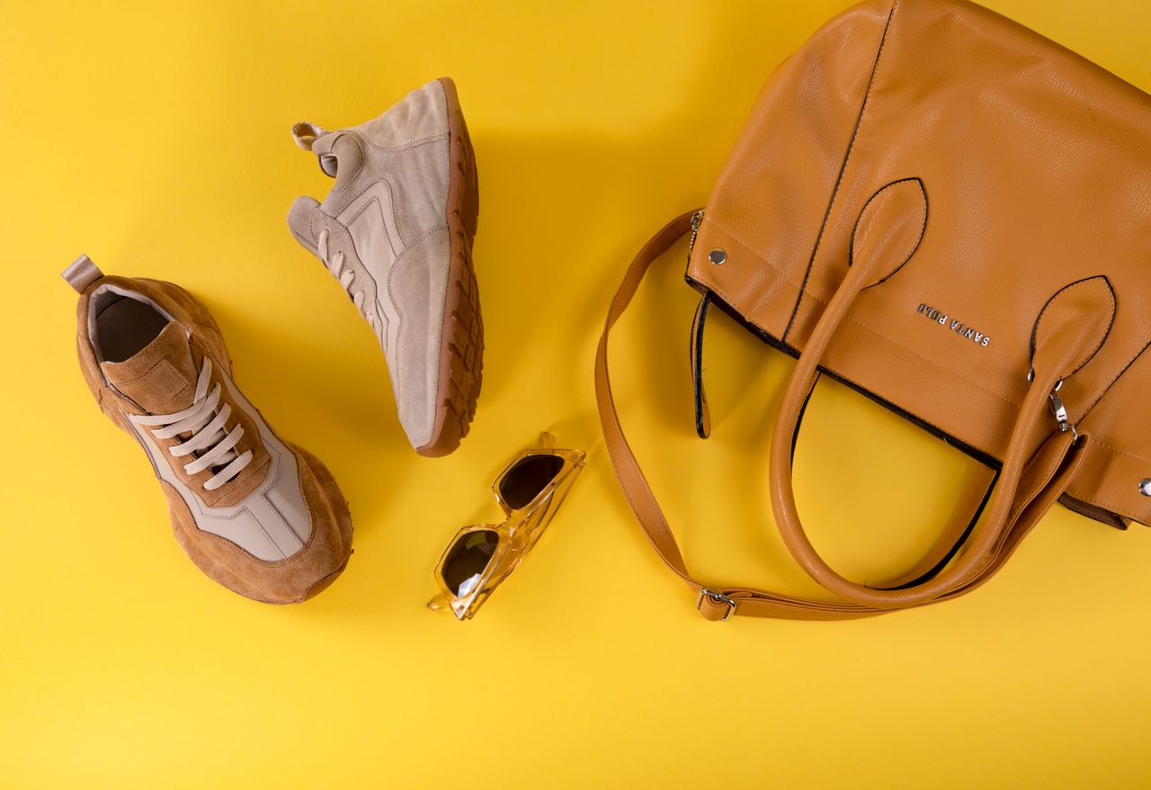about-bg Stylish brown handbag, fashionable eyewear, and sport shoes on vibrant yellow background.