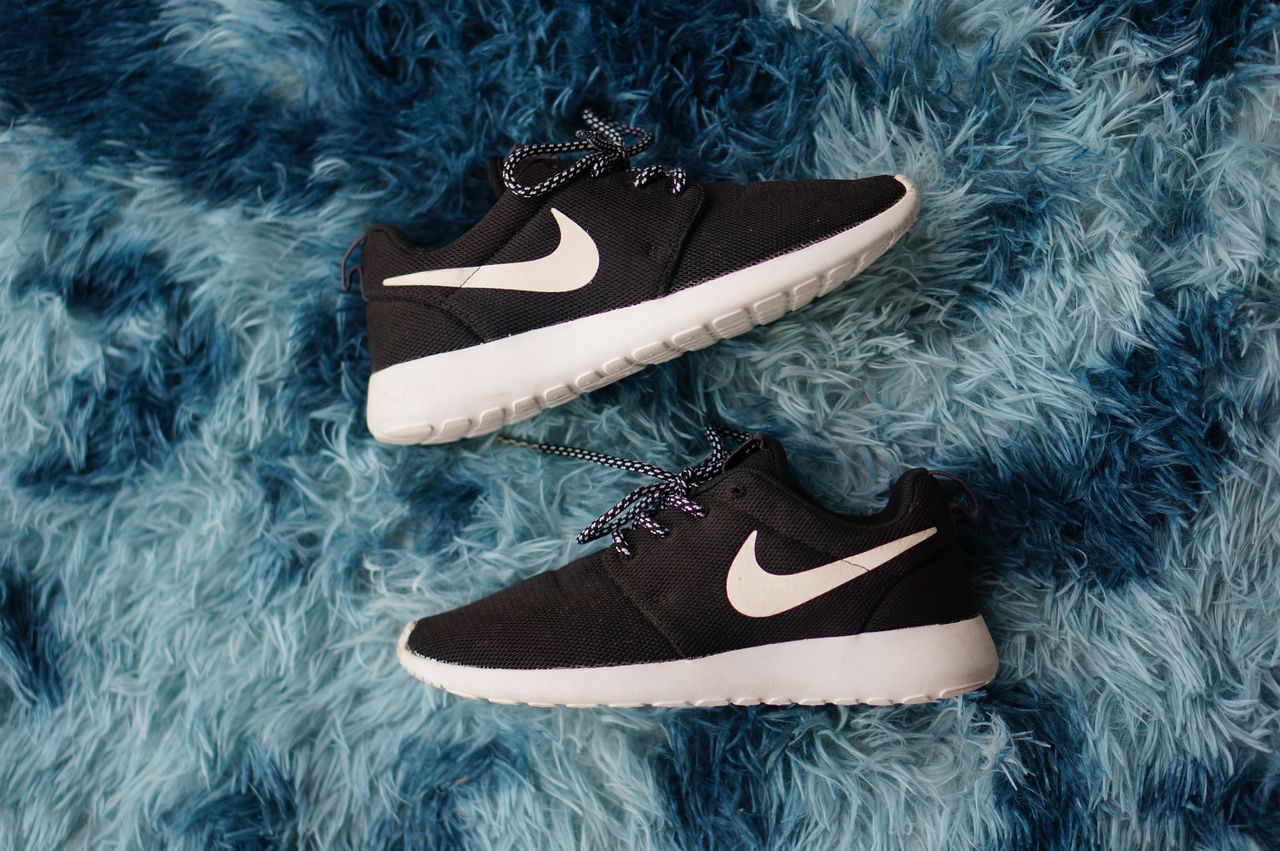 our-story Top view of black sneakers on textured blue fluffy rug, showing stylish footwear design.